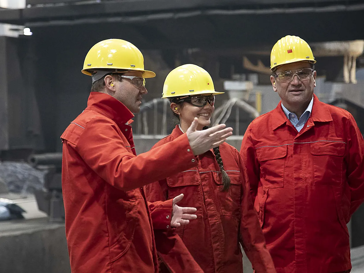 Arbeitssicherheit – Team mit Schutzhelmen bei der Begehung im Stahlwerk